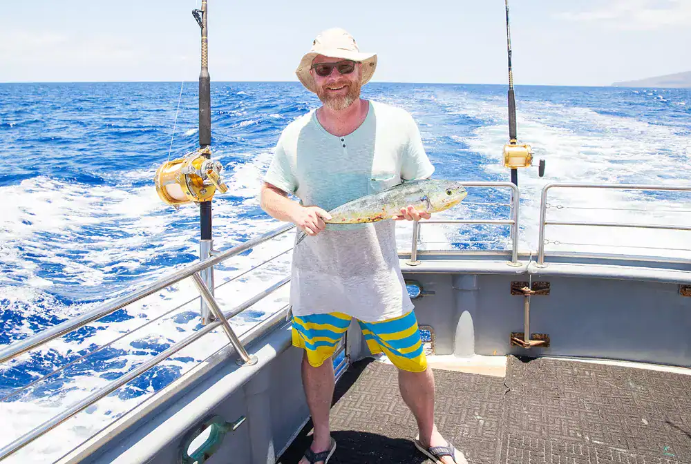 Man holding a fish on a boat during a fishing trip at sea.