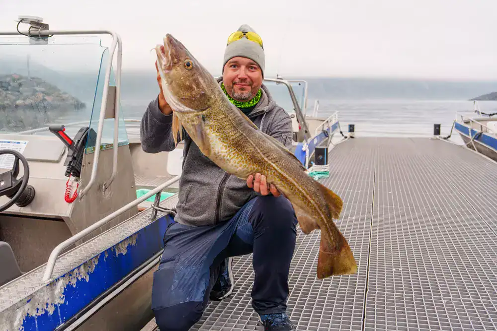 Man holding a large fish on a boat dock, Pacific fishing adventure.